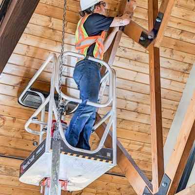 Worker using ReechCraft PowerLift platform to perform maintenance on a high wooden ceiling with exposed beams inside a building.