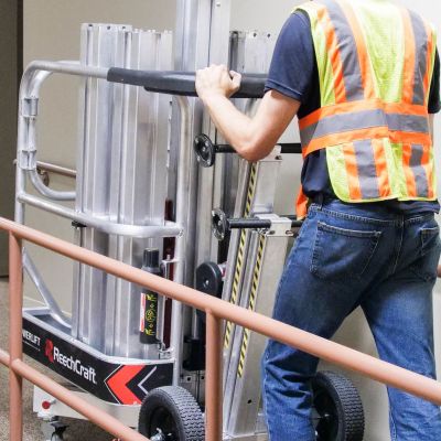 Worker maneuvering ReechCraft PowerLift through an indoor hallway using transport wheels and handle for easy positioning