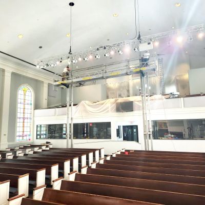 ReechCraft PowerMast freestanding system with extended platform installed inside a church sanctuary, positioned above pews for ceiling and lighting maintenance near stained glass windows.