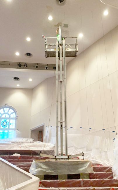 ReechCraft PowerMast freestanding system positioned on covered steps inside a church, with extended platform reaching high ceiling for lighting or maintenance work.