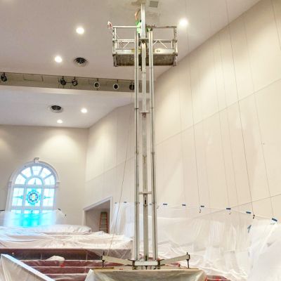 ReechCraft PowerMast freestanding system positioned on covered steps inside a church, with extended platform reaching high ceiling for lighting or maintenance work.