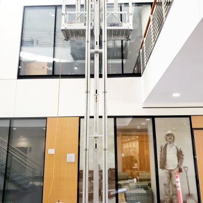 ReechCraft PowerMast freestanding system installed in a multi-story atrium, with dual mast configuration and extended work platform positioned near upper-level windows.