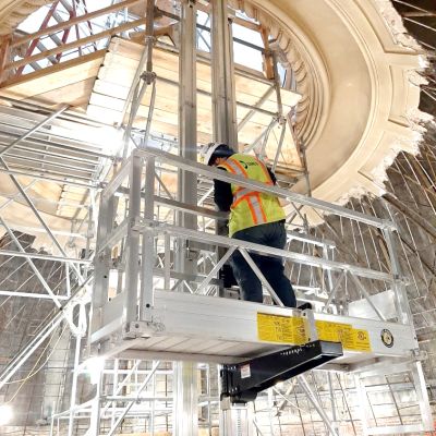 Worker standing on ReechCraft PowerMast platform inside a historic building dome, performing restoration work with scaffolding surrounding the structure.