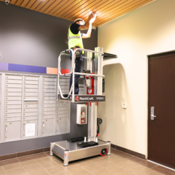 A worker is elevated on a PowerLift platform near the ceiling, performing maintenance or installation work.