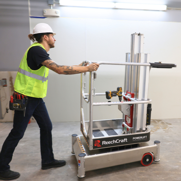 Worker wearing a hard hat and safety vest pushing a ReechCraft PowerLift lift system in an indoor construction area.